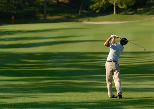 Man swinging a golf club on a golf course.