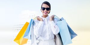 Woman wearing sunglasses and smiling holding shopping bags over both shoulders