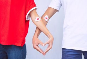 Two people attending a blood drive form a heart with their hands.