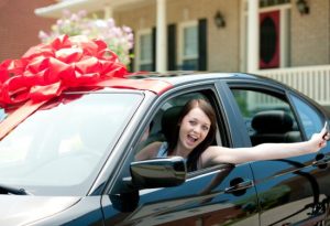 A girl enjoys her new car with a red bow on it.