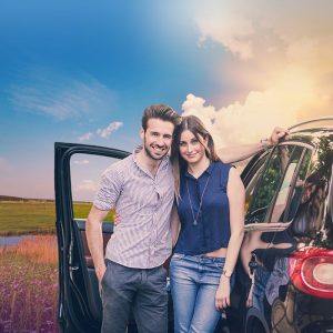Couple standing in front of a sport utility vehicle in front of a beautiful sunset.