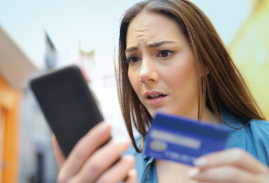 A young woman looks at her phone for fraudulent activity on her card.