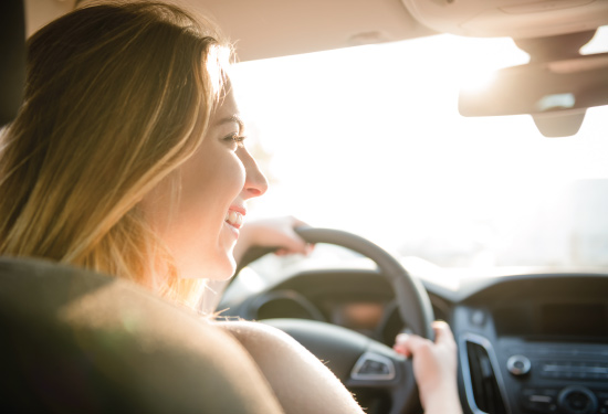 female driver smiling with sunshine in background