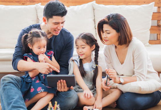 asian american family sitting together on floor looking at tablet together and smiling and laughing