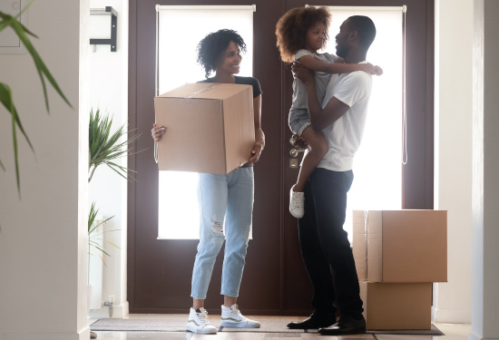 african american family moving into their newly purchased home, carrying in boxes in entryway and smiling