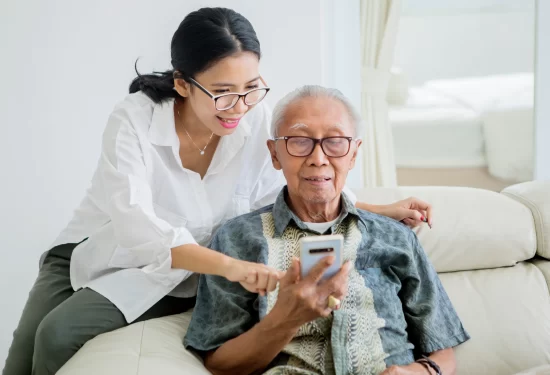 A woman is helping an older man with something on his phone.