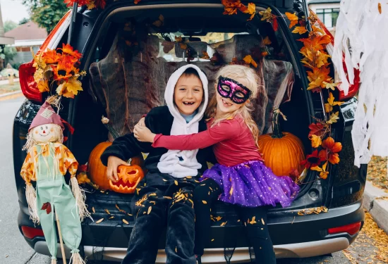 Two kids sit in the trunk of a car with halloween decorations.