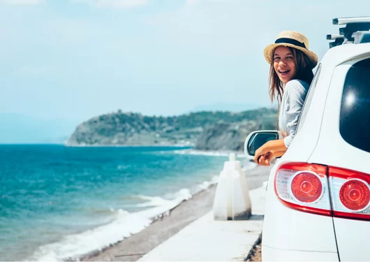 Girl riding in a car with her head leaning out of the window near the ocean.