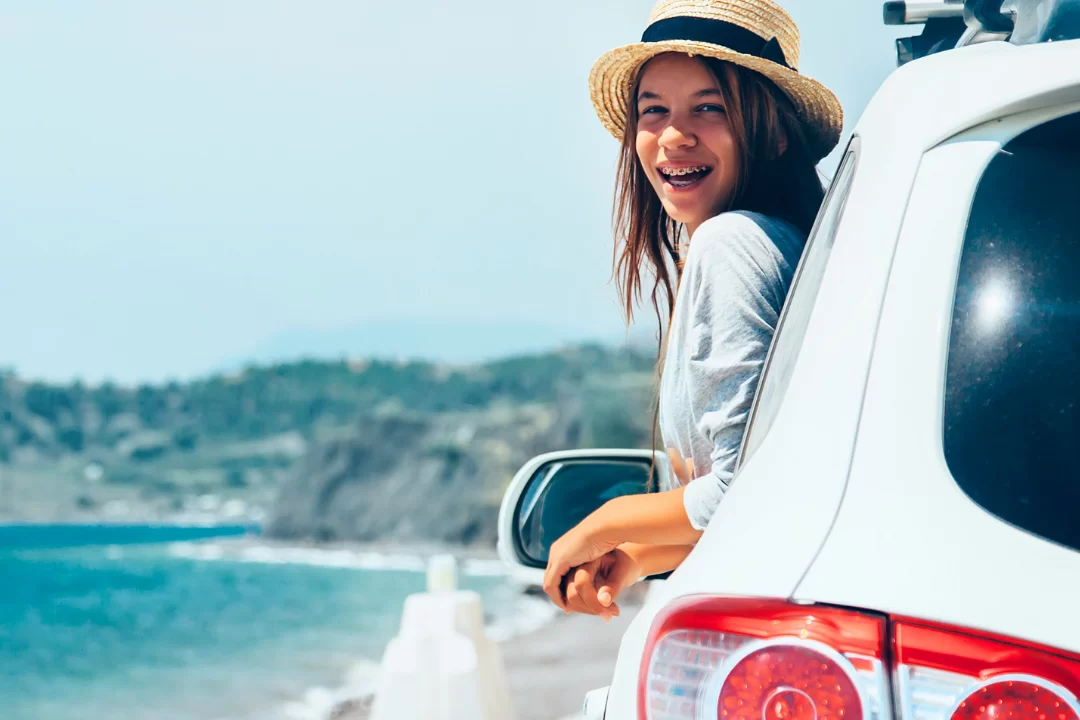 Girl riding in a car with her head leaning out of the window near the ocean.
